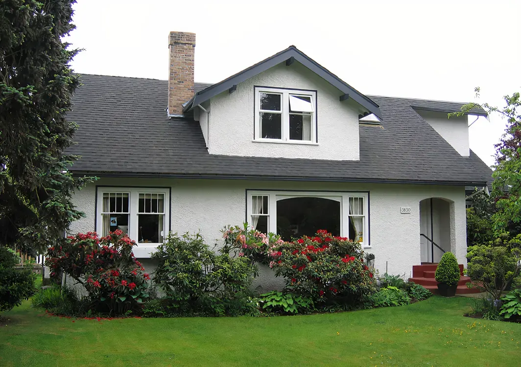 Crisp white exterior painting on a Vancouver heritage bungalow with dark trim and vibrant garden landscaping.