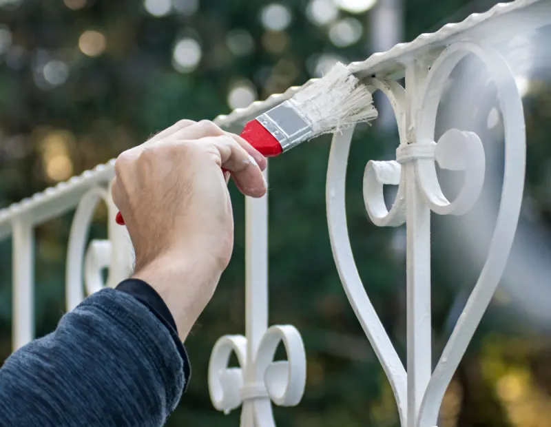 A contractor is painting a metal fence in a white colour.
