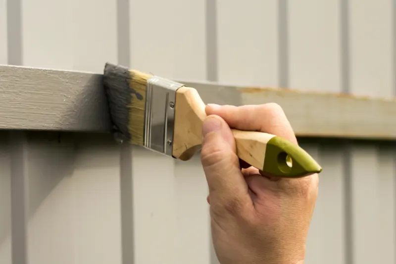 A contractor is finishing painting a wooden fence section.