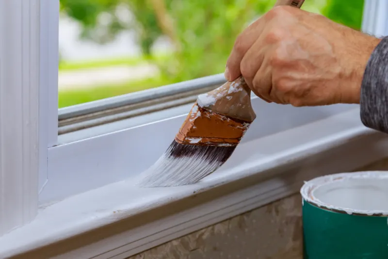 A contractor is using latex paint for a windowsill.
