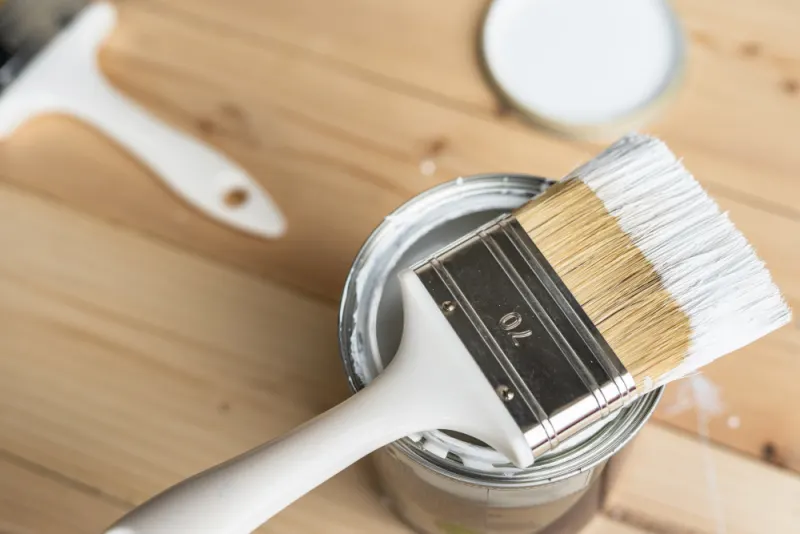 The brush has been dipped in the acrylic white paint and now is laying on the can.