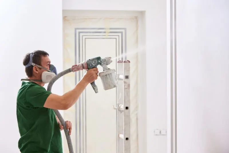 A man is spray painting interior house walls.