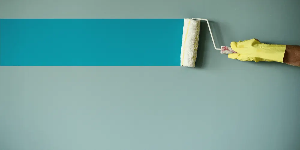 A hand in a glove painted a blue stripe on a wall with a roller.
