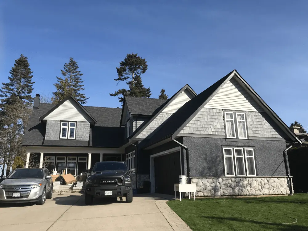 A big house with a black and grey exterior walls and 2 cars in a driveway.