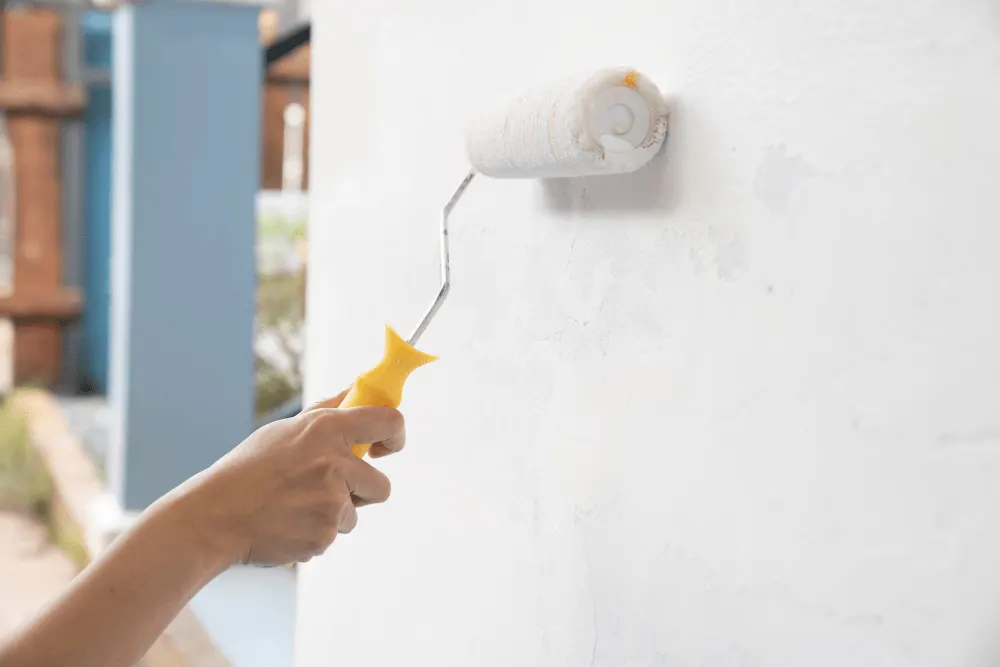 A hand with a painting roller is painting an exterior wall in a white colour.