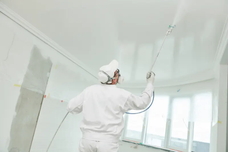 The painting contractor is spray painting a celling in a white colour.