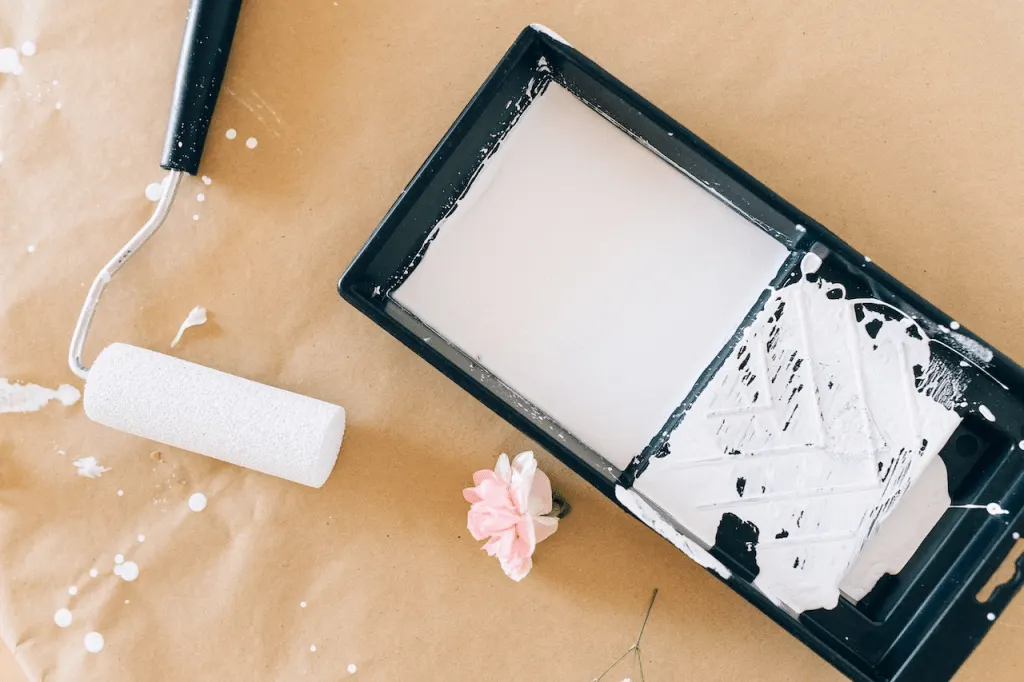 A painting roller and a tray with a white paint and a flower.