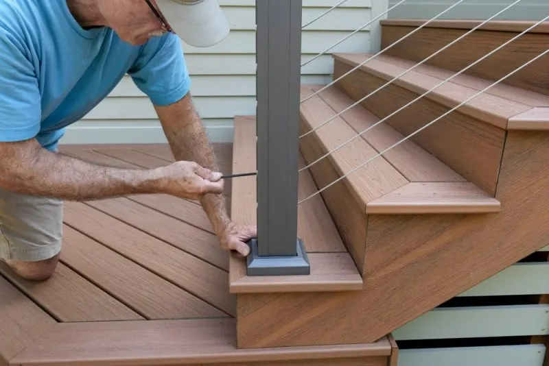 An old contractor is repairing stair railing with a screwdriver.