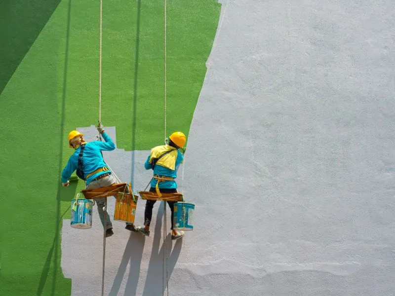 2 painters are painting grey wall in a green colour.