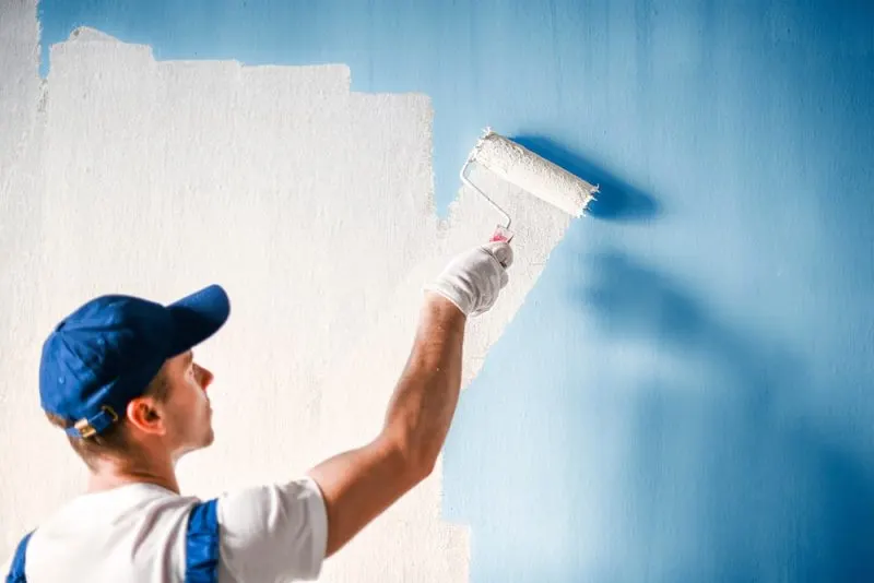 The painting contractor is painting a blue wall in a white colour.