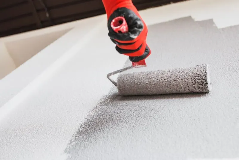 A painter is painting a white wall in grey with a painting roller.