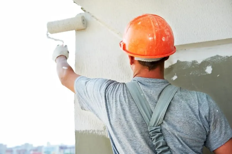 The painting contractor is painting an exterior wall in a white colour.