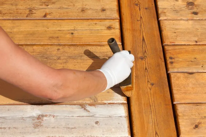 Person wearing a white glove applying varnish to a wooden deck with a brush.