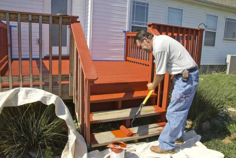 A painting contractor is painting the wooden stairs in a bright red color with a paint roller.