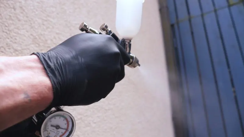 A man's hand in a black glove with an active paint sprayer.