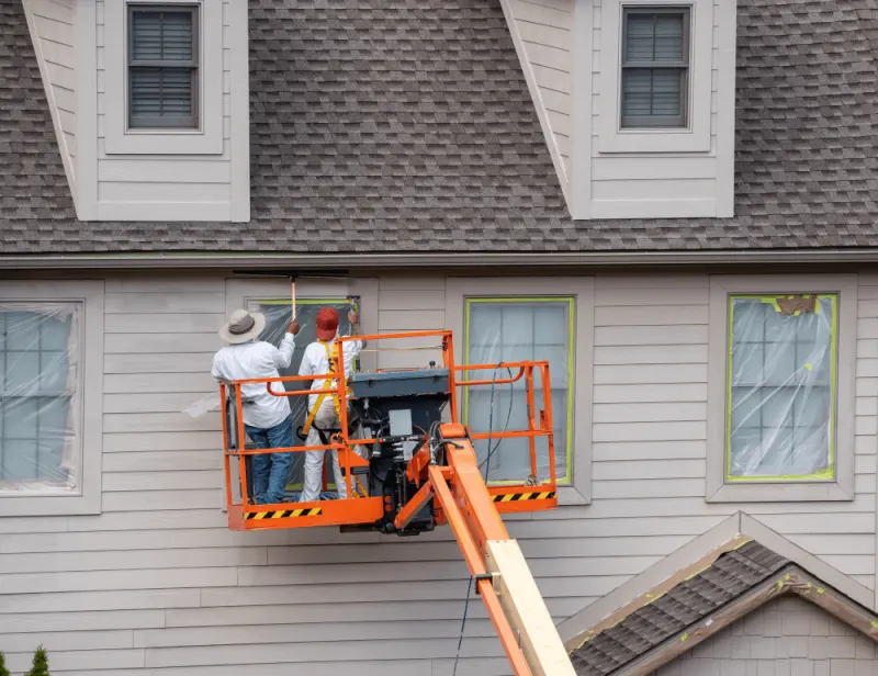 Two painters on a lift are painting house exterior wall in a boom lift.