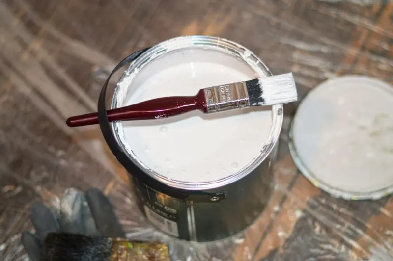 A white paint can with a brush on top.