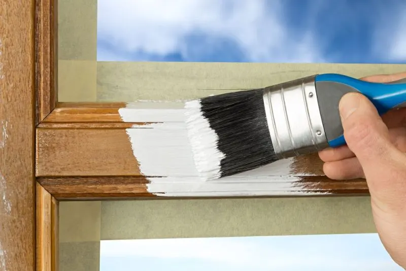 A man painting a window frame in white.