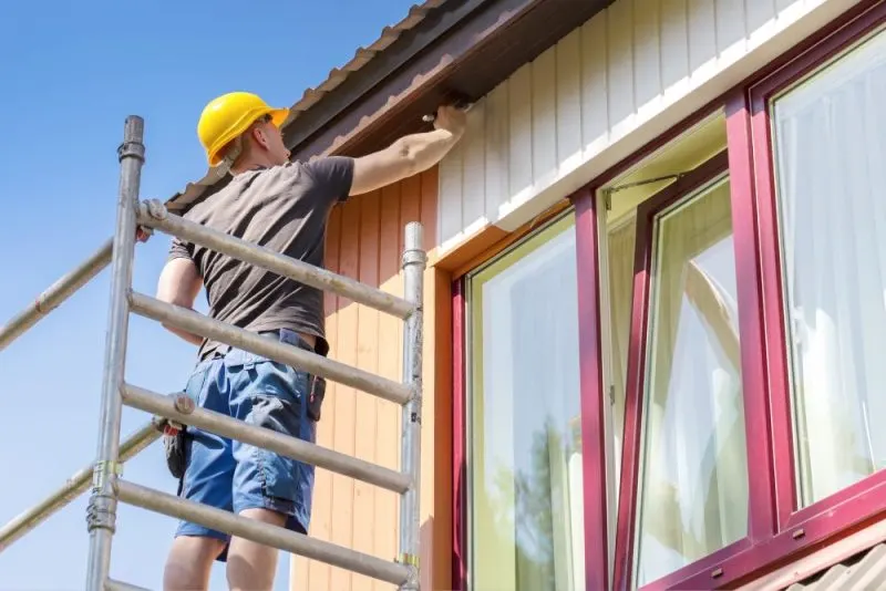 Exterior painter paints a house on scaffolding.