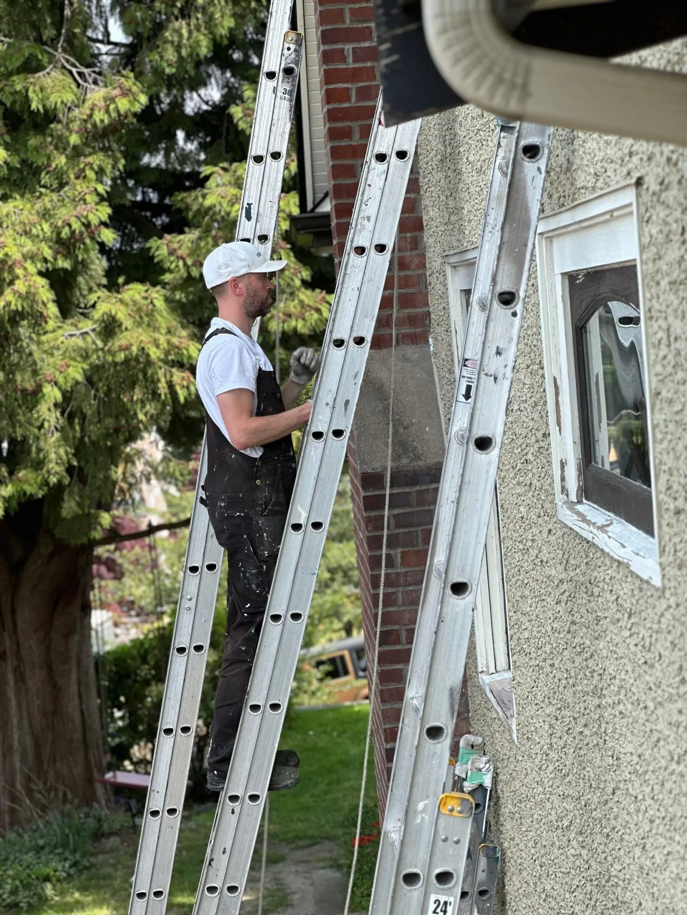 A painter is painting a stucco exterior stucco wall on a ladder.