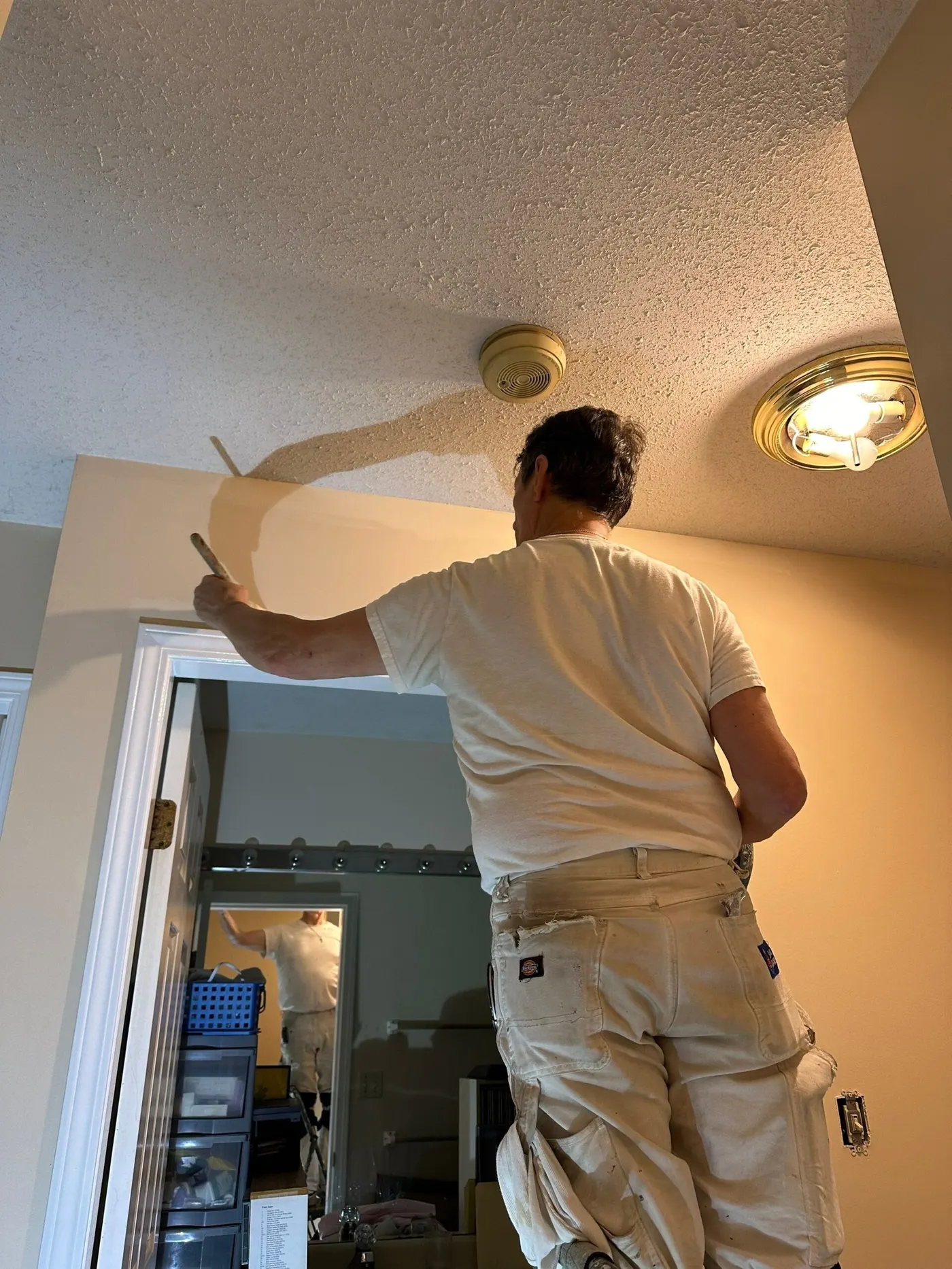 A painter in a dark white t-shirt is painting a door TOP in a white colour.