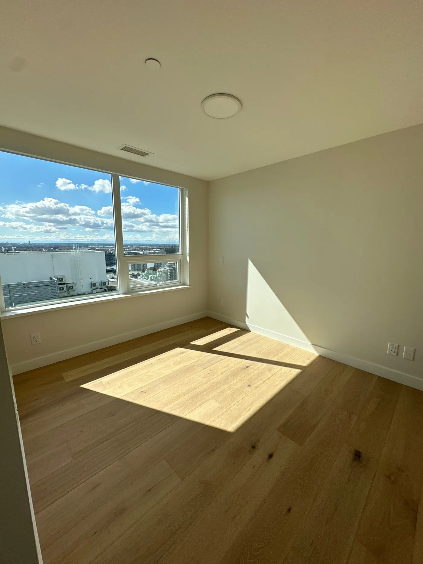 Sunlit room with large windows, light wood floors, and smooth white walls. Perfect for demonstrating expert drywall finishing and painting.