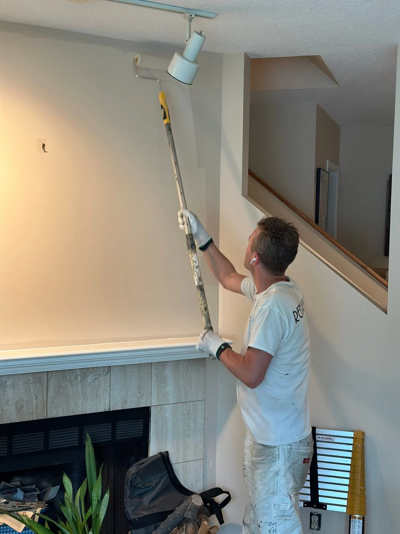 Professional painter applying a smooth coat of neutral paint with a roller on an interior wall.