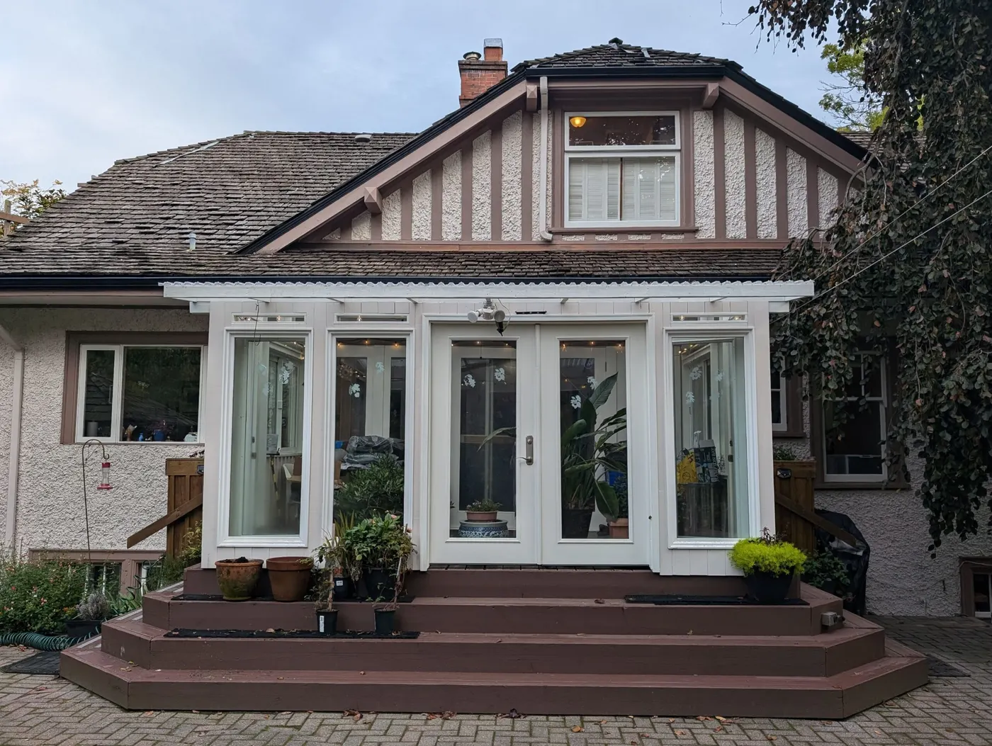 Back view of a traditional Vancouver home with white-framed sunroom, textured stucco walls, and brown wood steps with potted plants