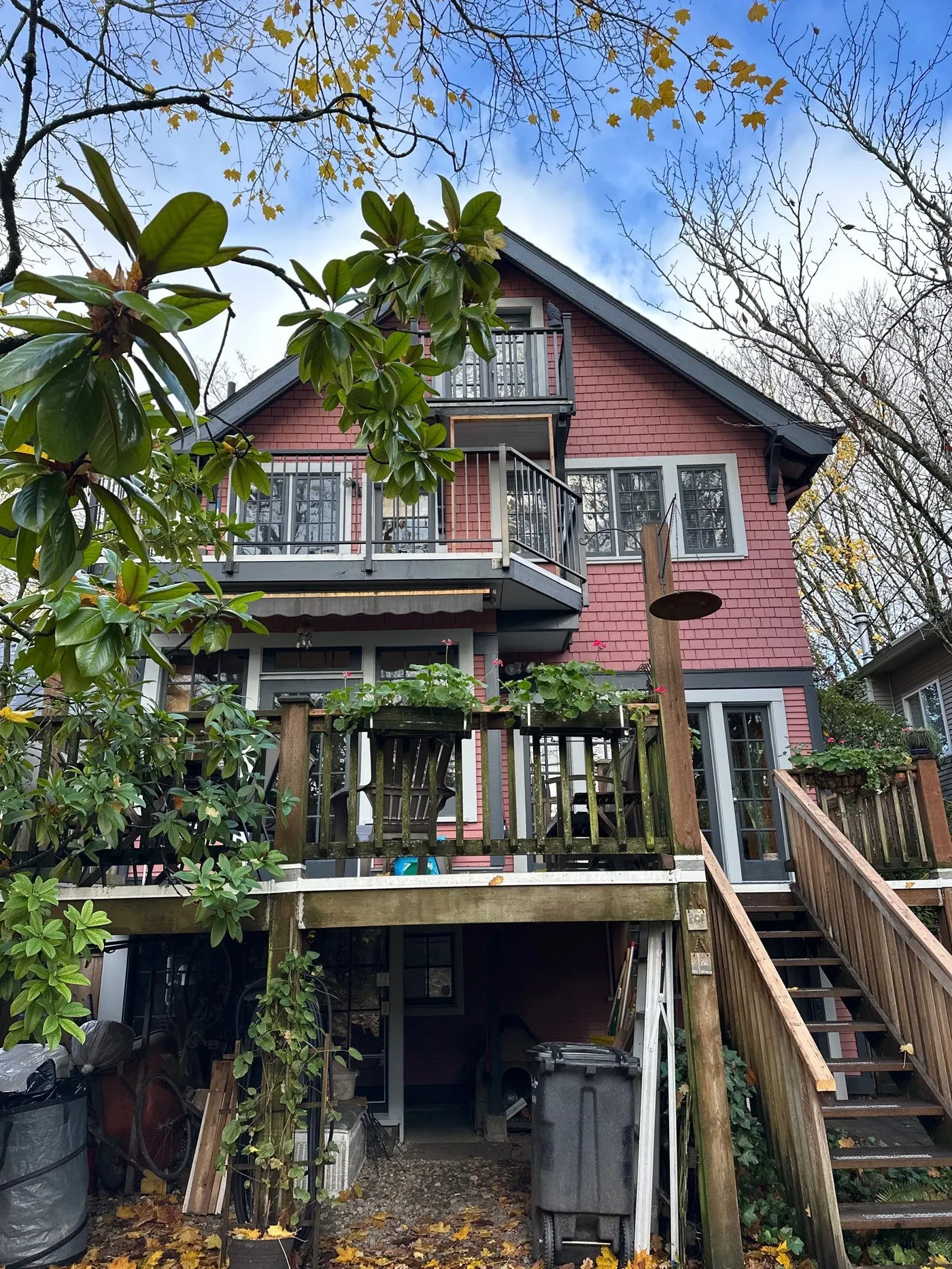 Back view of a three-storey Craftsman-style house with red shingle siding, wood deck, and surrounding autumn foliage.