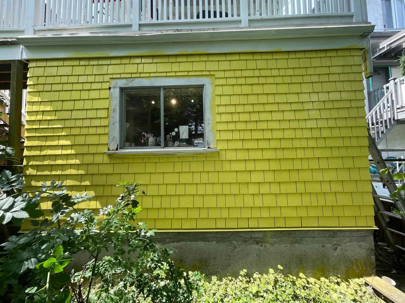 Freshly painted bright yellow shingle siding with white-trimmed window on a Vancouver, BC residential exterior.