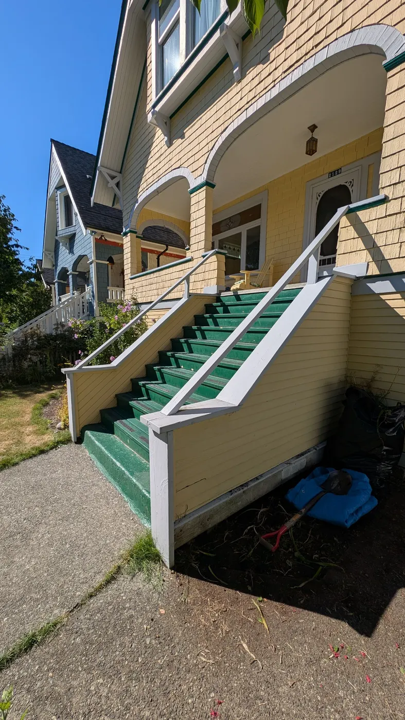 Front-facing view of a worn wood staircase leading to a covered porch on a yellow Vancouver heritage house, prior to repairs