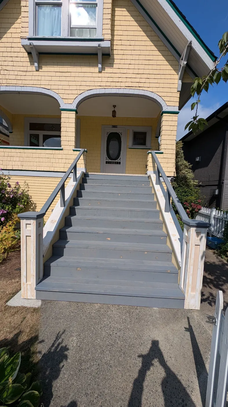 Completed front staircase in gray with white railings and posts leading up to a yellow Craftsman-style home's covered porch in Vancouver