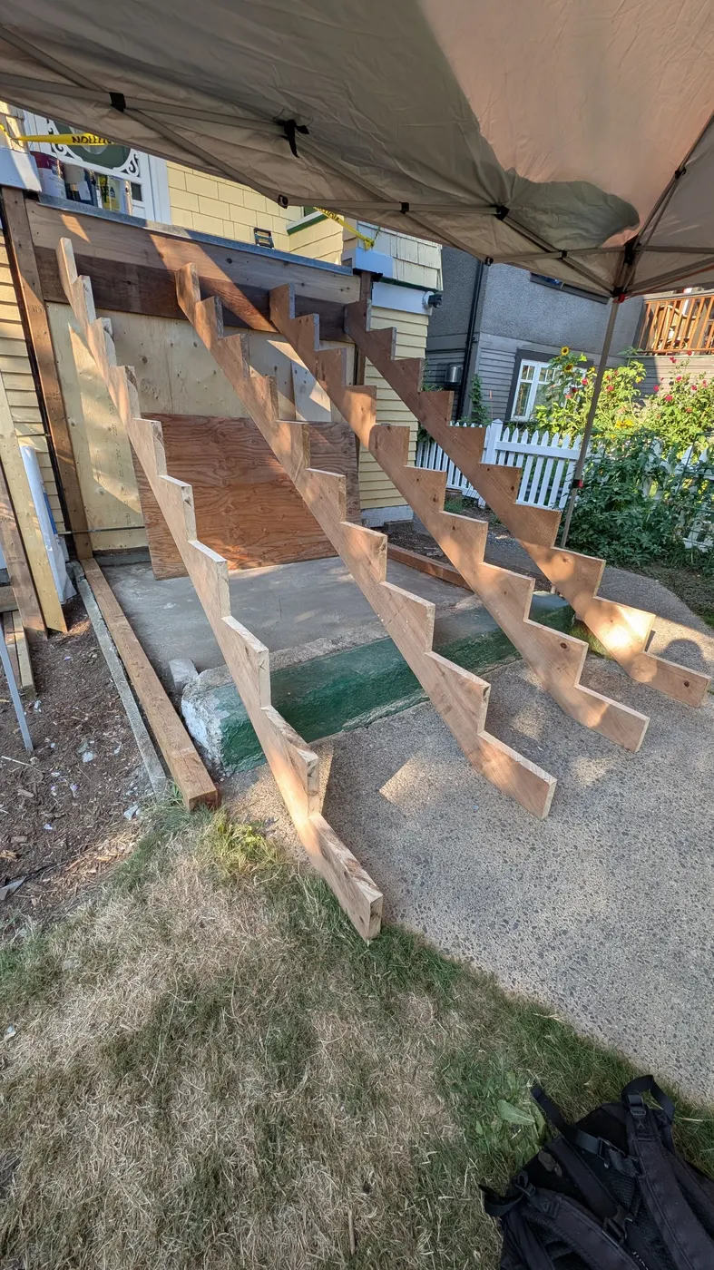 New wood stair stringers under construction beneath a weather tent at a Vancouver residential jobsite, framed for a rebuilt front staircase