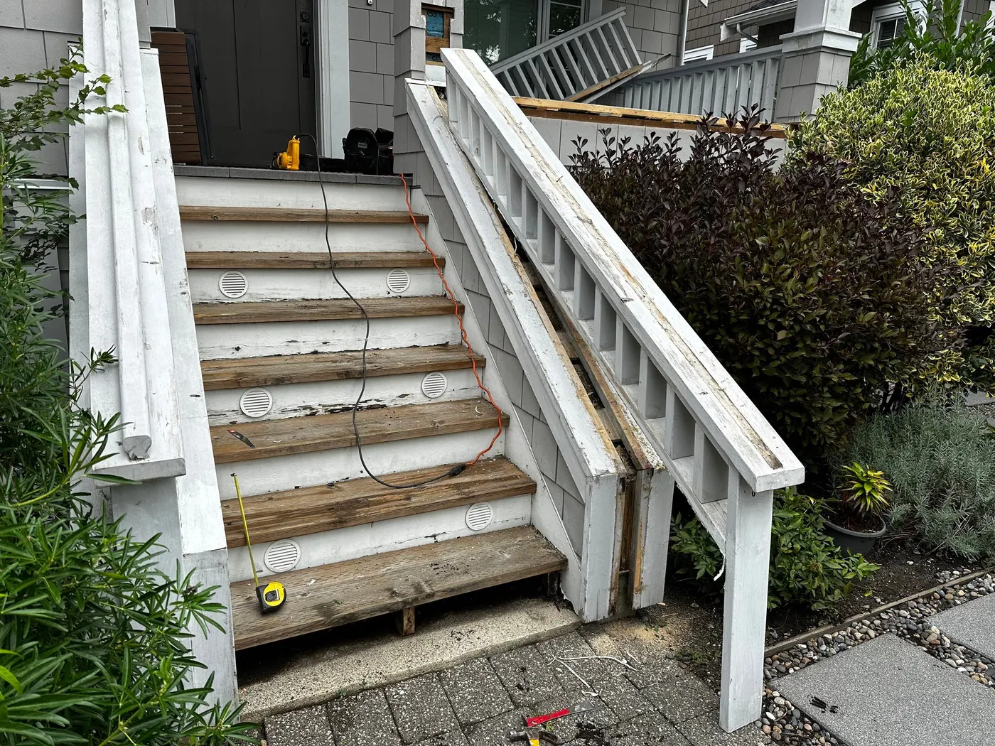 Front entry staircase in Vancouver, BC with old railings removed and worn wooden treads exposed during a carpentry demolition phase.