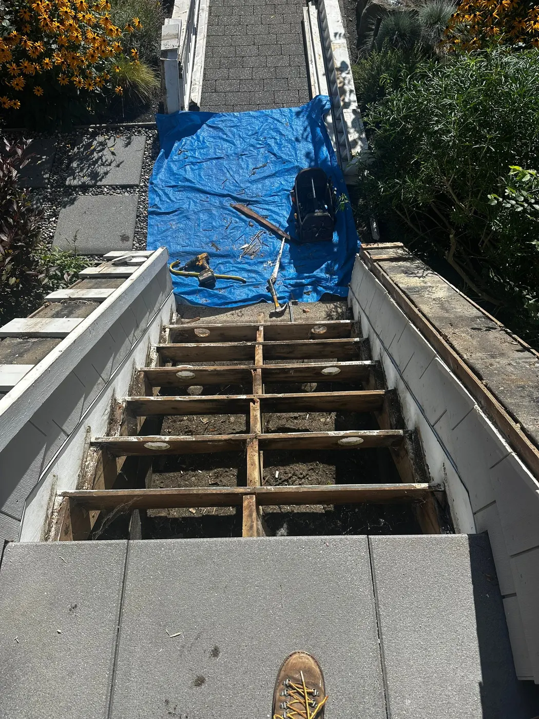 Side view of a Vancouver, BC front staircase with the white wood railing detached and leaning against the hedge during renovation.