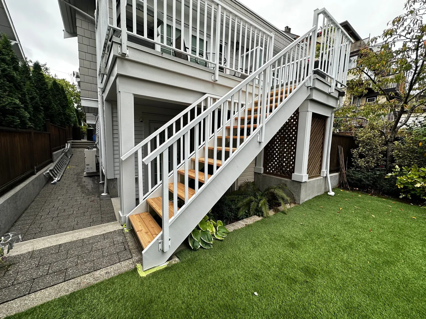 Newly rebuilt rear deck staircase in Vancouver, BC with white painted railings and natural cedar treads leading down to the yard.