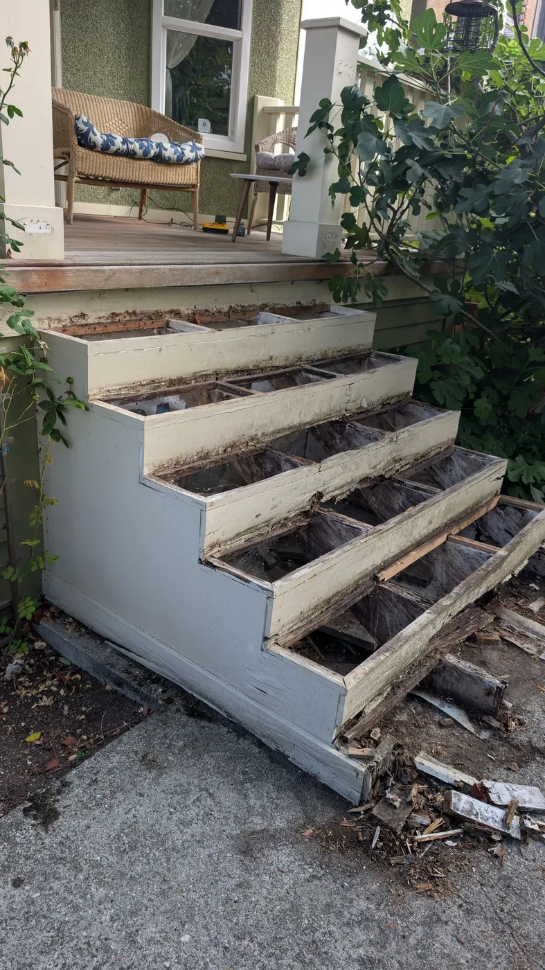 Underside view of rotted stair stringers and open risers exposed during demolition of a porch staircase in Vancouver, BC.