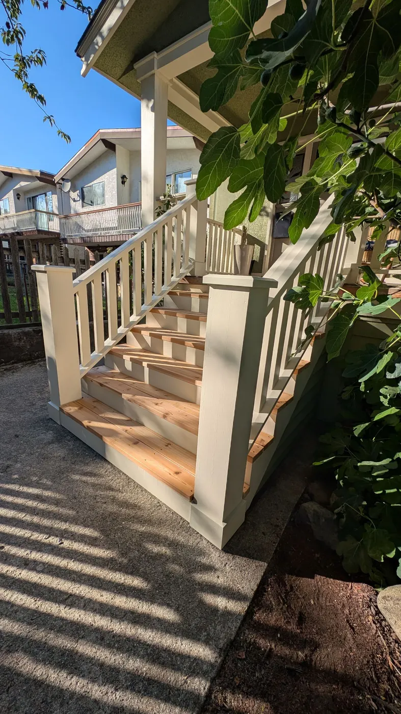 Angled view of a completed front porch staircase with new cedar treads and white railings at a Vancouver, BC home.