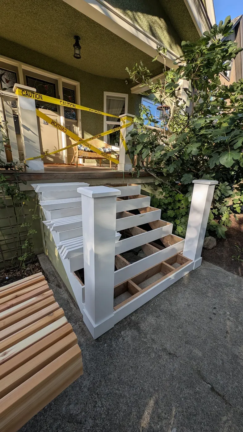 Painted white stair railings and newel posts installed on a rebuilt porch staircase, with cedar boards staged nearby, Vancouver, BC.