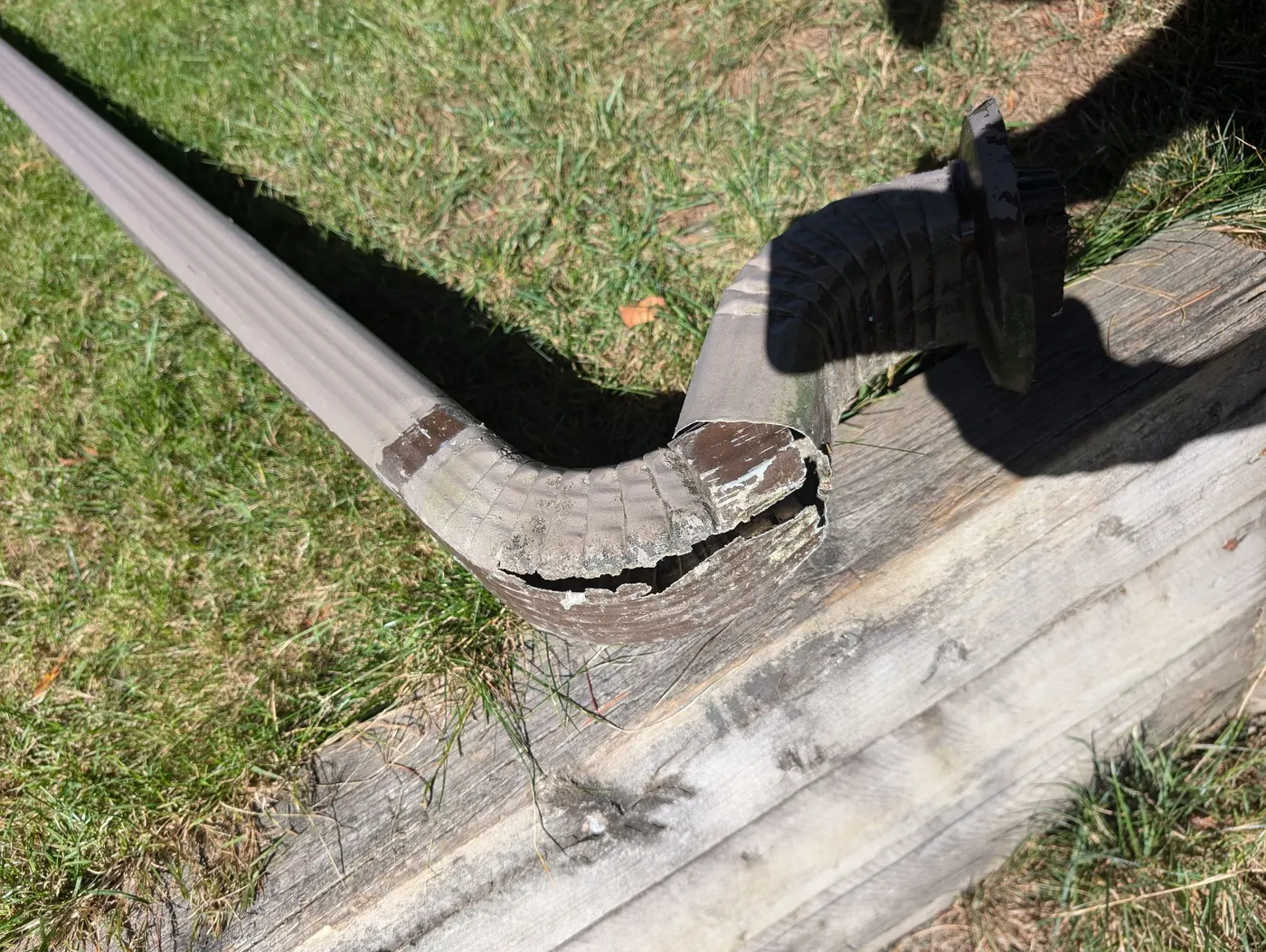 Close-up of a cracked and weathered aluminum downspout elbow on a Vancouver, BC home needing repair.