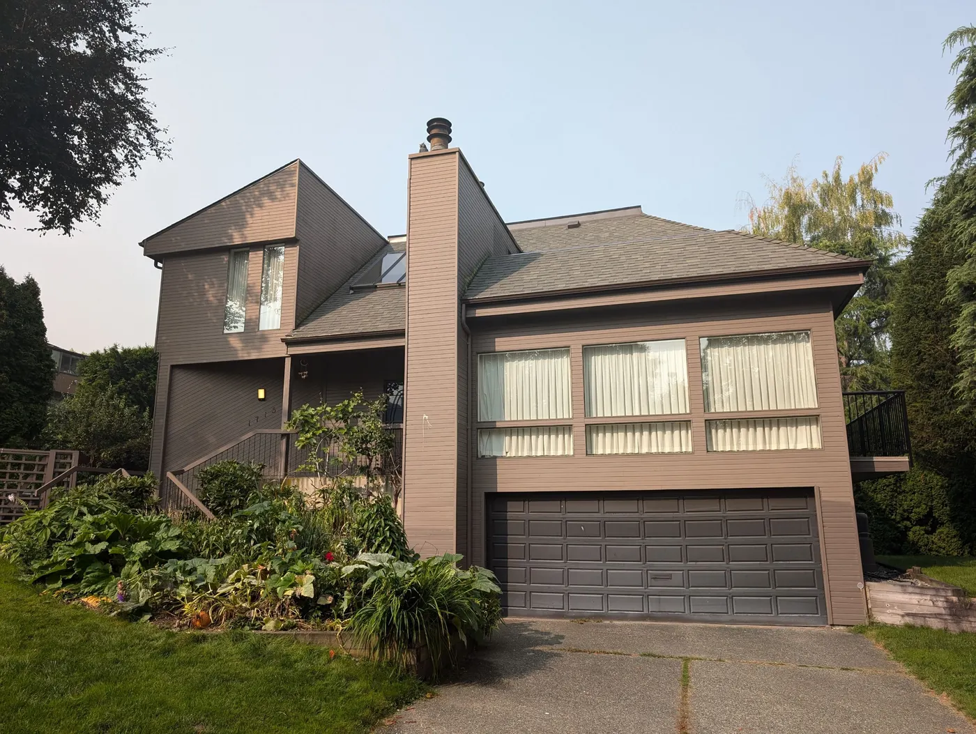 Two-story house exterior in Vancouver, BC freshly painted in warm taupe with a dark brown garage door and covered entry, completed by Renaissance Painting.