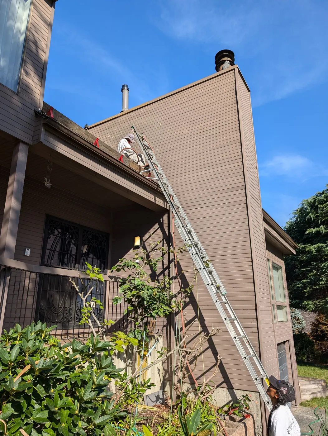 Painter on an extension ladder applying paint to a chimney on a two-story Vancouver, BC home.