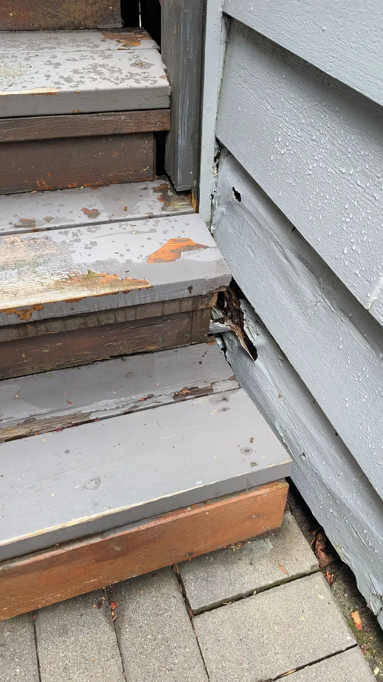 Weathered exterior wood stairs in Vancouver, BC with peeling paint and a rotted siding corner exposing decay beneath
