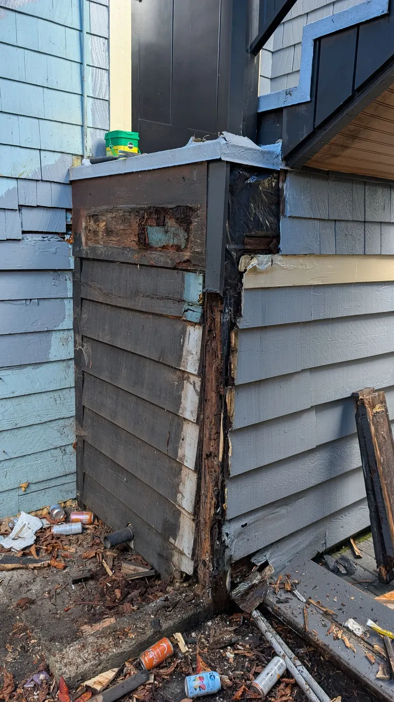 Severely water-damaged wood corner post and siding on a Vancouver house exposing rot beneath a staircase