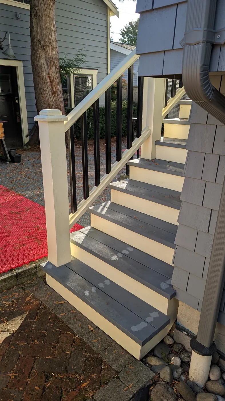 Side view of a repaired and repainted exterior staircase with black balusters against grey shingle siding, Vancouver BC.