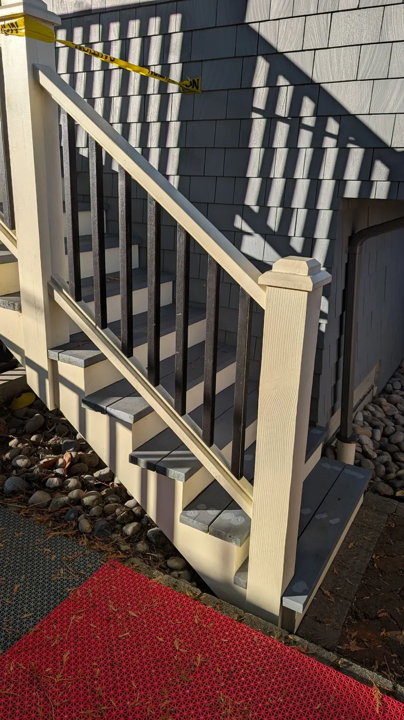 Wide-angle view of a finished exterior staircase repair with cream railings and grey shingle siding on a Vancouver, BC home.