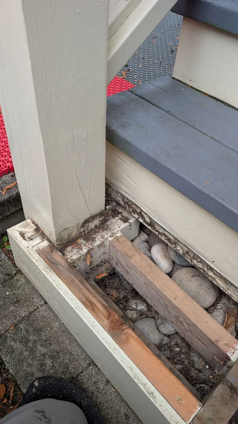 Close-up of a rotted deck post base and exposed rock footing on a Vancouver, BC exterior staircase before carpentry repair.