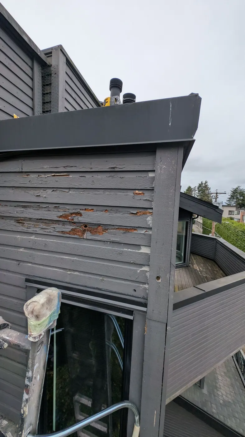 Close-up of rotted and cracked wood siding boards exposing bare wood on a Vancouver strata building roofline.