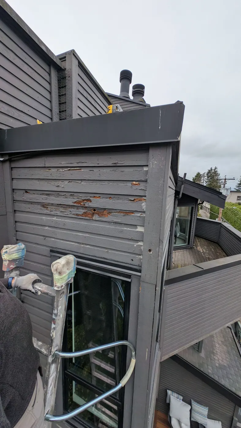 Detailed view of rotted wood siding with peeling paint and exposed grain on a Vancouver, BC strata building corner.