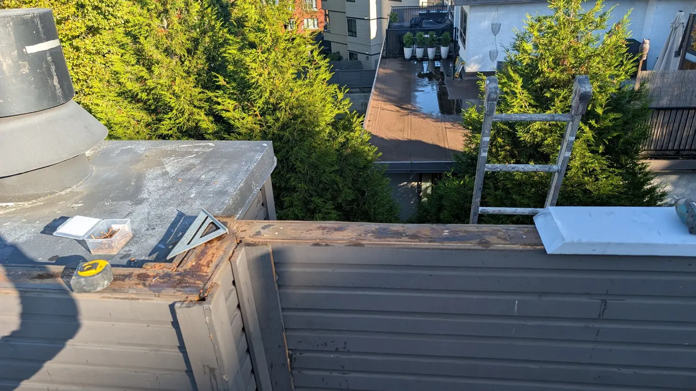 Carpenter installing painted wood parapet cap trim on a Vancouver rooftop deck with tools and square